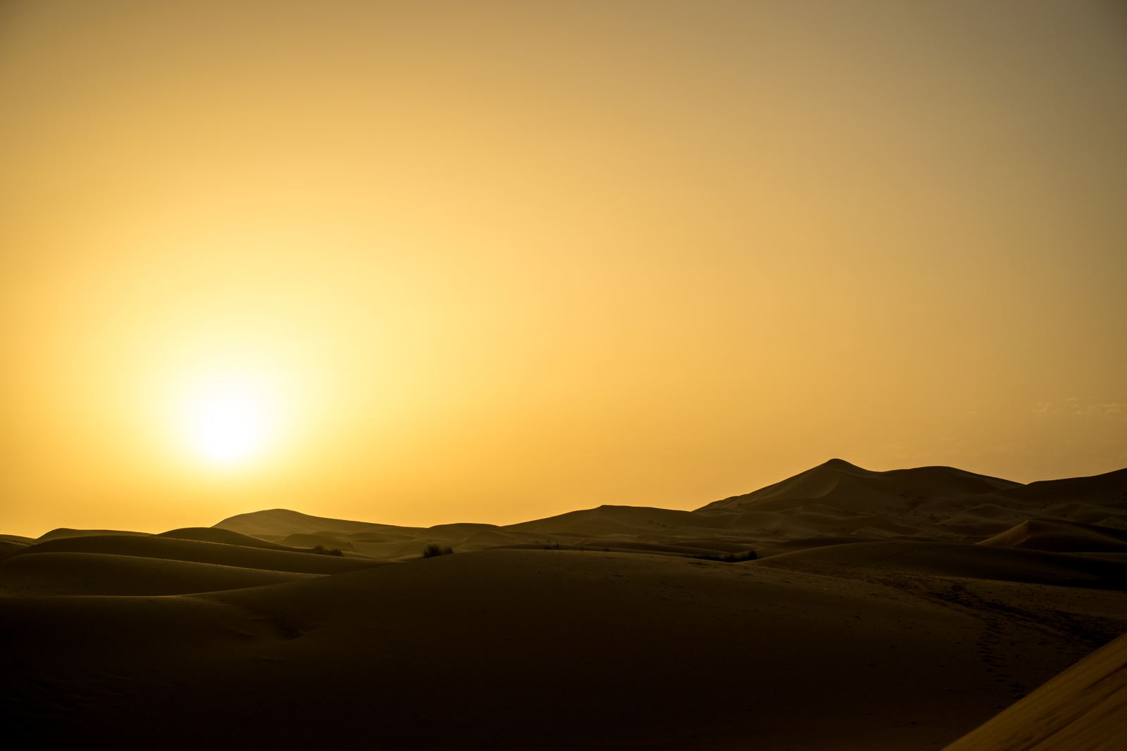 The sun rising over dark desert hills.